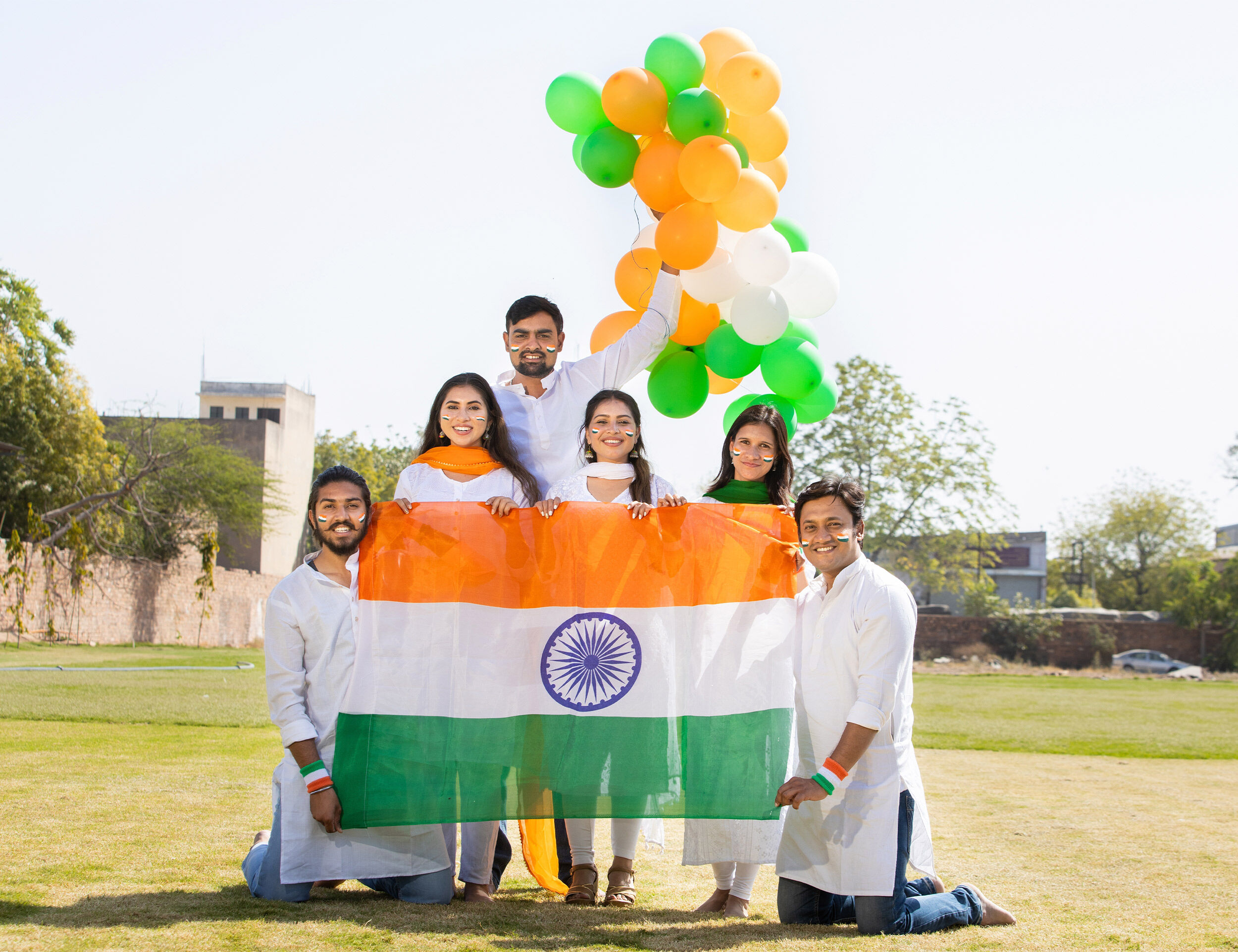 Group of young Indians celebrating Independence Day with the national flag and tricolor balloons in traditional white outfits on an open ground
